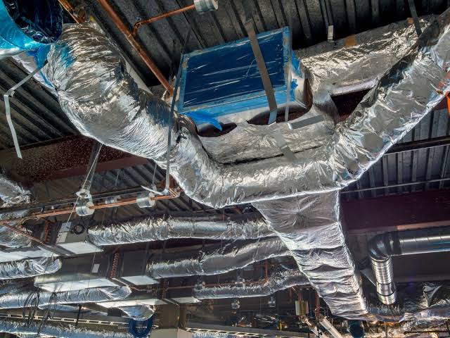 Insulated HVAC ductwork wrapped in a foil jacket in a commercial mechanical space.