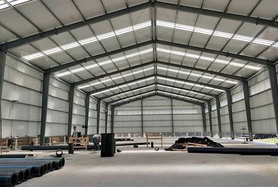 Interior of a pre-engineered building with roof sheeting overhead and pipe materials on site.